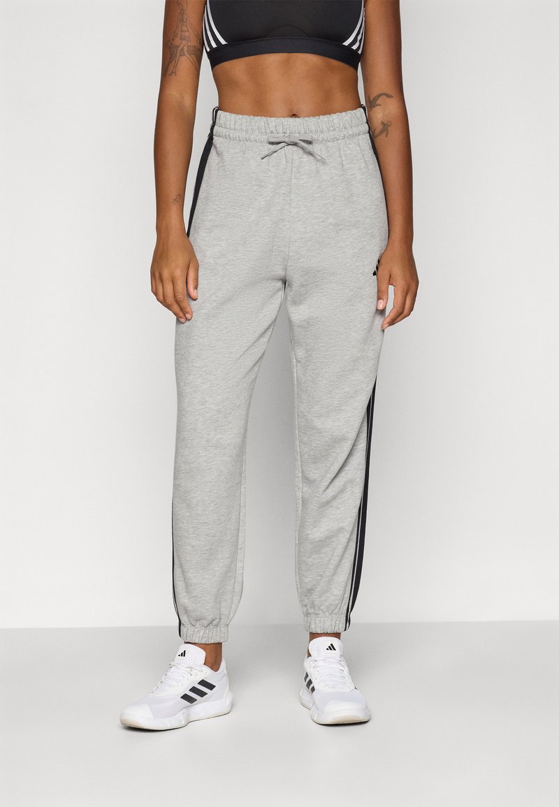 Lys grå joggebukser med svarte sidestreker, elastisk midje med snor, og tapered cuffs. Kombinert med hvite treningssko.