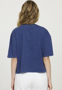 T-shirt oversize en denim bleu, avec manches courtes, col rond et ourlet court. Le tissu a une apparence légèrement texturée.