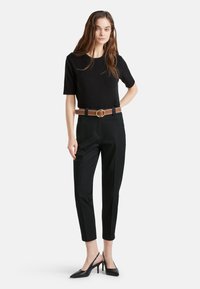 Czarna bluzka z krótkim rękawem zestawiona z dopasowanymi czarnymi spodniami i brązowym paskiem z okrągłą metalową klamrą. Czarne szpilki dopełniają stylizację.