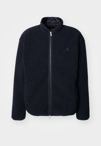 Giacca in pile blu scuro con colletto alto, chiusura con zip e dettagli del logo. Texture morbida e maniche lunghe, adatta per un abbigliamento casual.