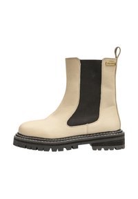 Bottine en cuir couleur crème avec des panneaux élastiques noirs sur les côtés, une languette de tirage et une semelle noire robuste. Présente un détail de couture.