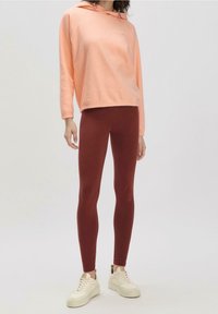 Felpa con cappuccio rosa chiaro con coulisse e polsini a coste abbinata a leggings aderenti color bordeaux e scarpe da ginnastica bianche. Tessuto morbido al tatto.