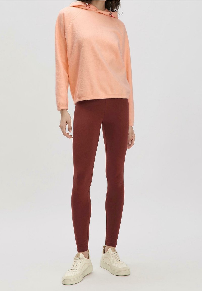 Felpa con cappuccio rosa chiaro con coulisse e polsini a coste abbinata a leggings aderenti color bordeaux e scarpe da ginnastica bianche. Tessuto morbido al tatto.