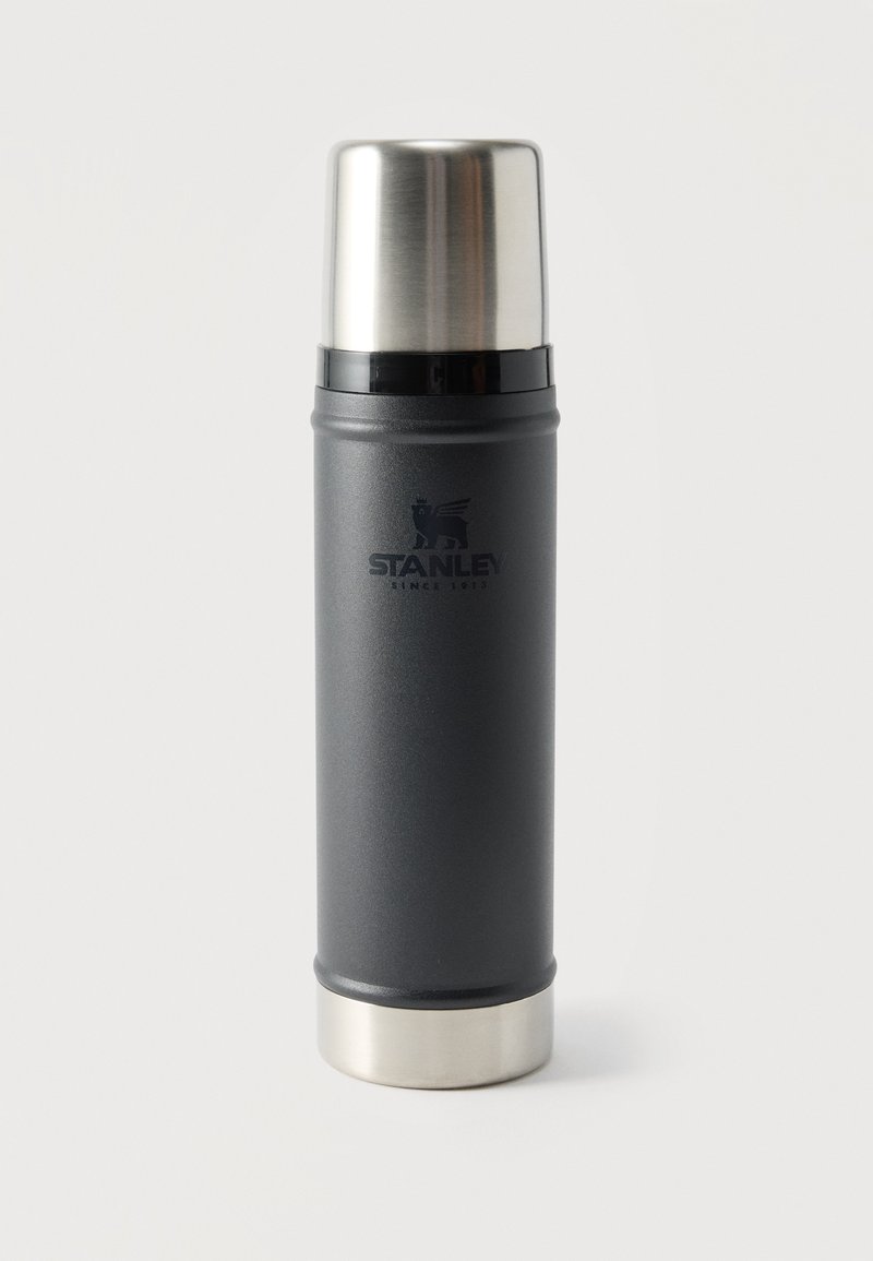Ψηλή μαύρη και ασημένια θερμός Stanley με αποσπώμενο καπάκι-κούπα, όρθια σε απλό λευκό φόντο.