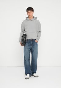 Grå hettegensere med lomme foran, kombinert med lyseblå vide bukser. Modellen holder en svart veske med metalldetaljer. Sneakers fullfører looken.