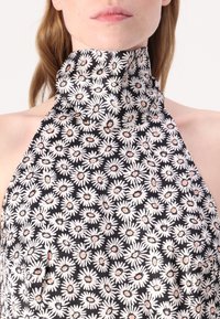 Ärmelloses Halfteroberteil mit hohem Kragen, gefertigt aus schwarzem Stoff, der mit weißen Gänseblümchen und pfirsichfarbenen Mittelpunkten verziert ist und ein florales Muster schafft.