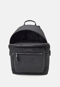 Sac à dos noir à motifs avec une poche avant zippée, un intérieur rembourré et une poignée supérieure. Présente des accents de logo et un design épuré.
