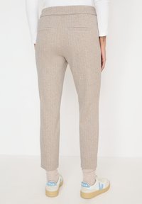 Světle béžové tapered kalhoty s texturovaným tkaním, dvěma zadními kapsami a elastickým pasem, doplněné o světlé tenisky a ponožky.