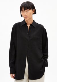 Schwarzes Langarmshirt aus leichtem Stoff, mit einem Button-Down-Kragen, Brusttasche und lockerer Passform. Glatte Textur.