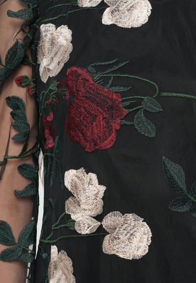 Zwarte stof met ingewikkelde bloemenborduursels in rode, crême en groene tinten, met gedetailleerde bladeren en een transparante textuur.