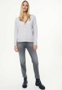Hellgrauer, strukturierter Cardigan mit V-Ausschnitt und vorderen Knöpfen, kombiniert mit grauen Jeans und schwarzen Ankle Boots.