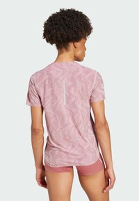 Camiseta atlética rosa de manga corta con un patrón en zigzag texturizado y una franja vertical reflectante en la parte posterior. Diseño ligero y ajustado.