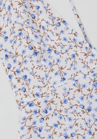 Tissu blanc avec petites fleurs bleues et des vignes brunes formant un motif floral dense et délicat sur un matériau texturé.