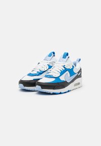 Scarpe da ginnastica Nike con un mix di materiali bianchi, azzurri e neri, dotate di una parte superiore in mesh testurizzato e ammortizzazione ad aria visibile nella suola.