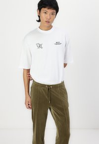 Weißes, übergroßes T-Shirt mit einem grafischen Druck auf der Brust, kombiniert mit olivgrünen, weichen Sweatpants mit Kordelzug und vertikalen Nähten.