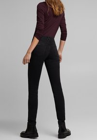 Jeans ajustados negros de cintura alta, con una textura suave y un detalle mínimo en los bolsillos traseros, combinados con botines negros.