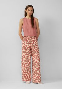 Rosa ärmelloses Oberteil kombiniert mit weiten Hosen mit einem beigen abstrakten Muster. Glatter Stoff, lässige Passform, dezente Textur und elastischer Bund.