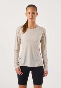 Beige atletisch shirt met lange mouwen van gestructureerde stof, ronde hals en platte naden. Gecombineerd met zwarte wielershorts. Blauw logo-accent.