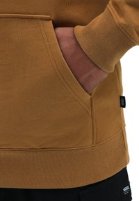 Brauner Sweatshirt mit Kängurutasche, gerippten Bündchen und Saum sowie einem kleinen schwarzen Etikett an der Seite, aus weichem Stoff gefertigt.