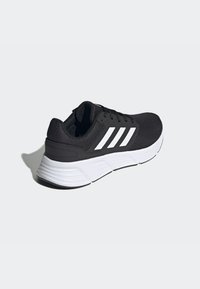 Scarpa da ginnastica nera con tomaia in mesh, logo a tre strisce bianche, suola ammortizzata e dettagli testurizzati sul tallone.