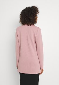 Długorękawowa odzież wykonana z miękkiego, różowego materiału, z okrągłym dekoltem i prostym krojem. Tekstura jest gładka, z delikatnym prążkowaniem.