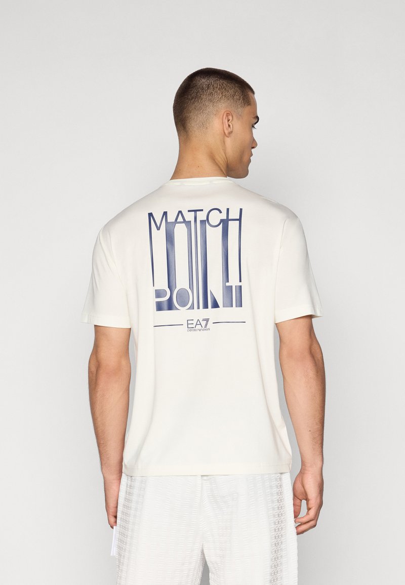 Kreminės spalvos trumpomis rankovėmis marškinėliai su tamsiai mėlynu grafiniu spaudiniu „MATCH POINT“ ant nugaros ir apvalia iškirpte.