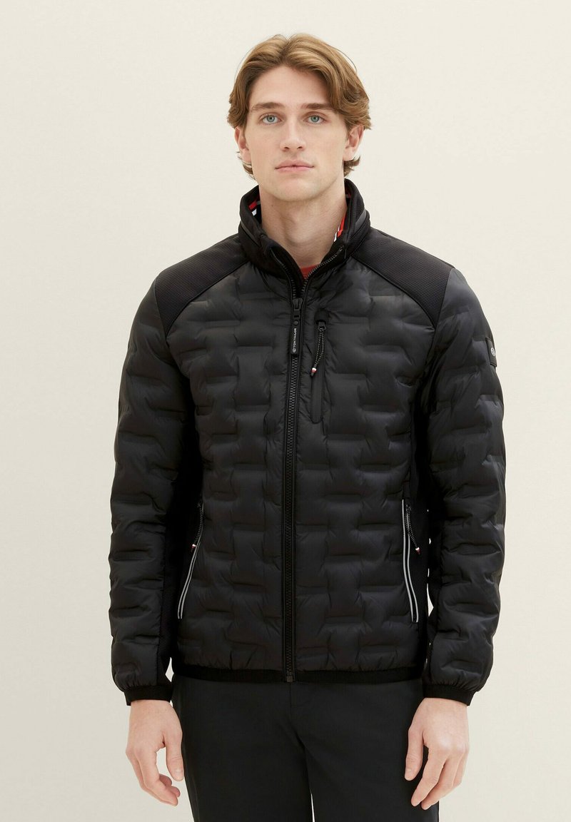 Giubbotto imbottito nero con design trapuntato, colletto alto e tasche con zip. Presenta accenti a contrasto sulle spalle e polsini elasticizzati.