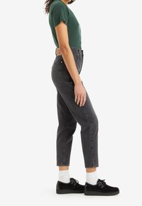 Höga svarta jeans med slim fit, bärs med en grön skjorta och svarta skor, med vita strumpor. Märkbar texturerad tyg och design.