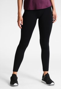 Czarne legginsy sportowe z gładkiego, elastycznego materiału, dopasowanym kroju i pełnej długości. Noszone z czarnymi butami sportowymi.