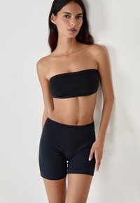 Top bandeau nero senza spalline e pantaloni shorts a vita alta, realizzati in un tessuto liscio e elastico, con un design senza cuciture e bordi puliti.