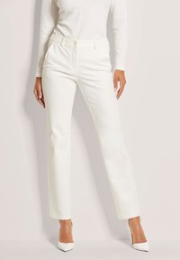 Witte op maat gemaakte broek met een recht model, knoopsluiting en zijzakken. Gemaakt van een gladde, gestructureerde stof, gecombineerd met puntige hakken.