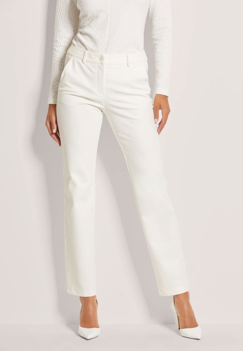 Witte op maat gemaakte broek met een recht model, knoopsluiting en zijzakken. Gemaakt van een gladde, gestructureerde stof, gecombineerd met puntige hakken.