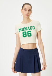 Kerman toppi vihreällä "MONACO 86" -grafiikalla; yhdistetty tummansiniseen laskostettuun hameeseen, joka on sileän tekstuurin ja rakenteellisen muotoilun omaava.