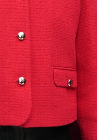 Κόκκινο υφασμάτινο σακάκι με τρία λαμπερά ασημένια κουμπιά, συμπεριλαμβανομένου ενός σε μια μικρή τσέπη με καπάκι στη δεξιά πλευρά μπροστά.