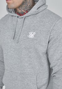 Gray hoodie made of soft fabric with a front pocket, drawstring hood, and a white embroidered logo on the left chest area.