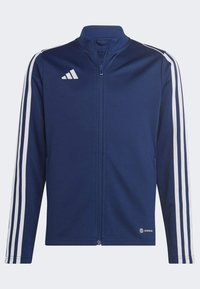 Marineblaue Sportjacke mit Reißverschluss aus glattem Stoff, mit weißen Streifen entlang der Ärmel und einem Adidas-Logo auf der Brust.