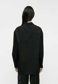 Camisa negra de manga larga con cuello y dobladillo recto. Tejido ligero con una textura suave, con puños abotonados y un corte relajado.