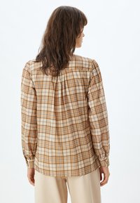 Bruine en beige geruite blouse met lange mouwen, geplooide details aan de achterkant en knoopmanchetten. Lichtgewicht stof en een ontspannen pasvorm.