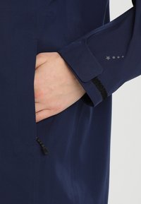 Navy blue waterproof jacket with smooth texture; features zippered pocket and Velcro cuff detail. Star pattern near sleeve opening.