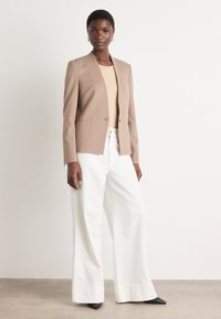 Light brown blazer with a single-button closure and front pockets, paired with white wide-leg trousers and black pointed-toe heels.
