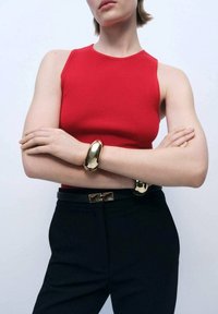Red ribbed tank top, black fitted trousers, metal bracelet with a smooth, shiny surface, and a black belt with a metallic clasp.