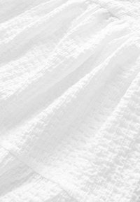 Texturerad vit tyg med synliga veck, med en skrynklig, rynkad ytdesign. Mjuk, lätt material med subtila mönster.