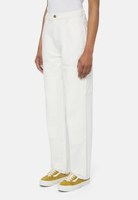 Vita vida byxor med hög midja, med sidofickor och en texturerad tyg. I kombination med gula sneakers.