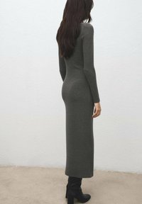 Lang, tætsiddende, mørkegrå kjole med lange ærmer og høj hals, lavet af et blødt, tekstureret stof, båret med knæhøje sorte støvler.