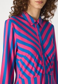 Robe chemise ajustée en tissu lisse, avec de larges rayures diagonales roses et bleues, un col et une fermeture à boutons sur le devant avec des poches poitrine.