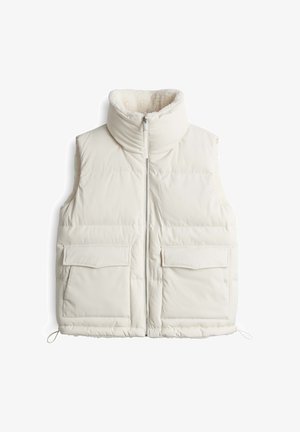 Gilet en duvet de couleur blanc cassé, avec un col haut, une fermeture zippée et deux poches plaquées à l'avant. Doublure douce et texturée pour plus de chaleur.
