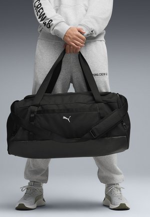 Svart duffelväska med justerbar axelrem, dragkedjor och en vit logotyp. Tillverkad av slitstarkt tyg med en jämn yta.