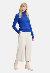 Kék garbó pulóver bordázott mandzsettákkal, krémszínű, széles szabású nadrággal és bézs bokacsizmával párosítva. Simára szőtt anyag, testhez álló fazon.