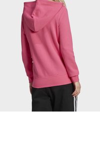 Růžová mikina z měkkého materiálu s kapucí na stahovací šňůrku, žebrovanými manžetami a lemem, s volným střihem, doplněná černými kalhotami.