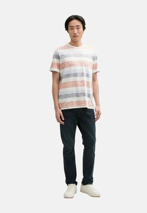 Camiseta a rayas con franjas horizontales rojas, azules y blancas, fabricada en material liviano. Combinada con jeans oscuros y zapatillas blancas.